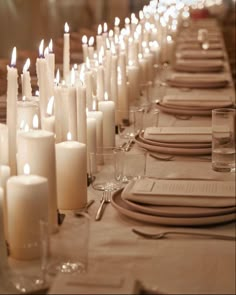 a long table is set with white candles and place settings for dinner guests to enjoy