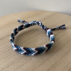 a close up of a bracelet on top of a wooden table with white and blue beads