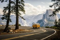 an orange van driving down a winding road with mountains in the background