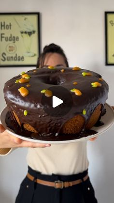 a woman holding a chocolate frosted cake on top of a white plate with green and yellow sprinkles