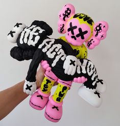 a hand holding a pink and black teddy bear with bones on it's back