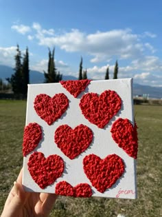 someone is holding up a piece of art made out of crocheted red hearts