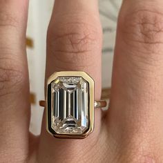 a close up of a person's hand wearing a ring with an emerald stone