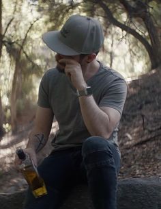 a man sitting on top of a tree trunk holding a beer in his right hand