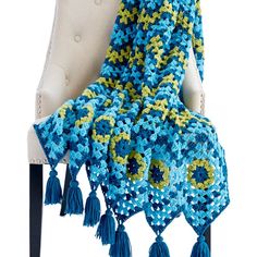 a blue and yellow crocheted blanket sitting on top of a chair with tassels