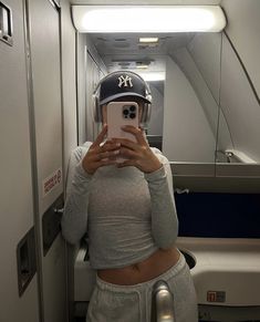 a woman taking a selfie in an airplane with headphones and a baseball cap