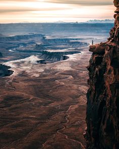 a person standing on the edge of a cliff looking out over a river and mountains