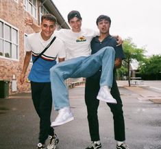 three young men posing for a photo in front of a brick building