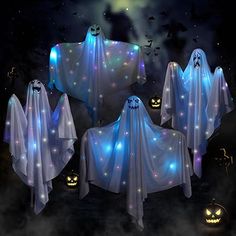 four ghost - like decorations in the dark with pumpkins and bats around them, all lit up at night