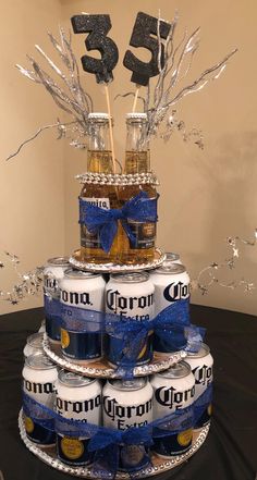 a cake made out of beer cans and decorated with blue ribbon, is sitting on top of a table