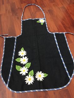 a black apron with white daisies and green leaves on the front, sitting on a wooden floor