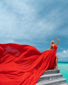 a woman in a red dress is standing on some steps near the ocean and posing for a photo