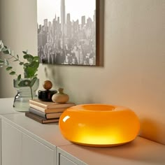 an orange light sitting on top of a white shelf next to a plant and books