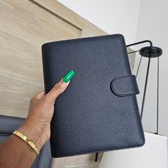 a hand holding a black leather notebook with a green marker on it and a lamp in the background