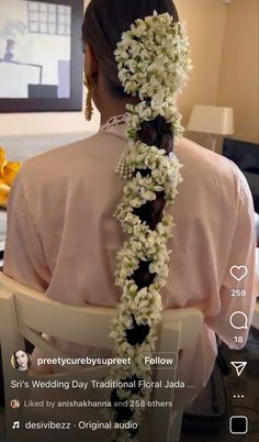 the back of a woman's head with flowers in her hair, sitting on a chair