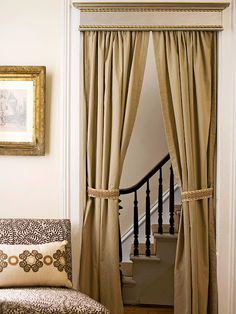 a living room filled with furniture and a window covered in draping next to a stair case