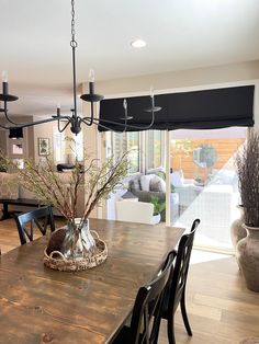 a dining room table with chairs and a vase on it's centerpiece in front of a sliding glass door