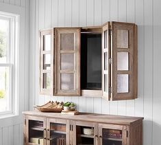 a wooden cabinet sitting next to a window in a living room with white walls and wood flooring