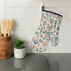 an oven mitt hanging on the wall next to a potted plant and wooden utensils