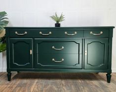 a dark green dresser with gold handles and knobs on the drawers is against a white wall