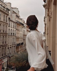 a woman is walking down the street with her hand in her pocket and looking at buildings