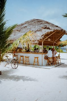 two people sitting at a bar on the beach with bikes parked in front of it