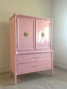 a pink armoire with two doors and three drawers on the front, against a white wall