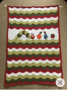 a crocheted blanket with apples and caterpillars on it, sitting on the floor