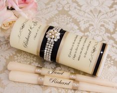 two ivory colored candles with black ribbon and pearls on them, sitting next to pink roses