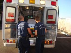 two emergency personnel loading an ambulance into the back of a truck