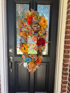 a colorful wreath on the front door of a brick house with an animal tag hanging from it's side