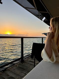 a woman sitting at a table on top of a boat watching the sun go down