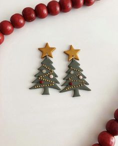 two wooden christmas trees with gold stars on them next to red beaded necklaces