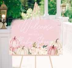 a welcome sign with pumpkins and flowers is displayed on an easel in front of a porch