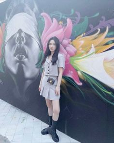 a woman standing in front of a wall with flowers painted on it