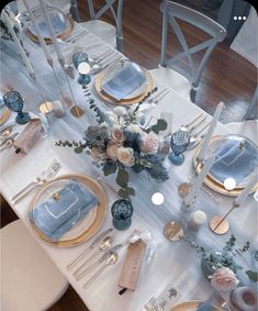 the table is set with blue and white plates, silverware, flowers and candles