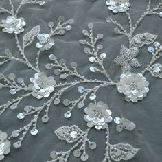 an embroidered fabric with silver flowers and leaves on grey mesh material, closeup view