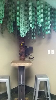 two metal stools sitting next to a wooden table with green ribbons hanging from it