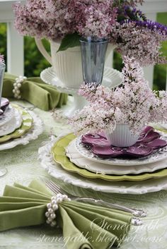 the table is set with purple flowers in vases and green napkins on it