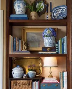 a bookshelf filled with blue and white vases next to a lamp on top of a table