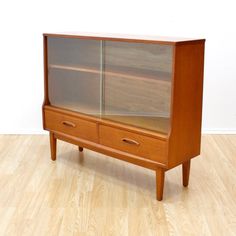 a wooden cabinet sitting on top of a hard wood floor next to a white wall