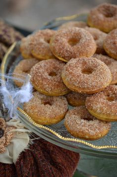 a plate full of sugared donuts on top of a glass platter with a cloth bag in the background