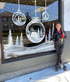 a woman standing in front of a store window with christmas decorations hanging from the windows