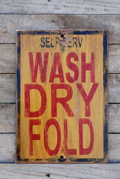 a yellow sign that says wash dry fold on the side of a wooden wall with red lettering