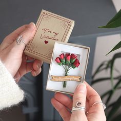 a woman is holding a small box with flowers in it and an engagement ring on her finger