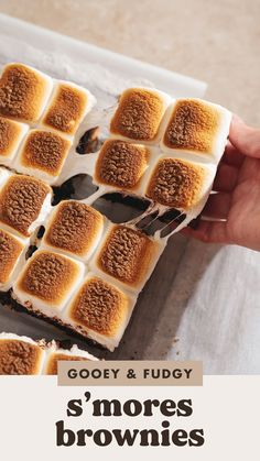 someone holding a piece of cake with marshmallows on it and the words gooey & fudy s'mores brownies