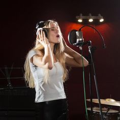 a woman with headphones standing in front of a microphone and holding her hands to her ears