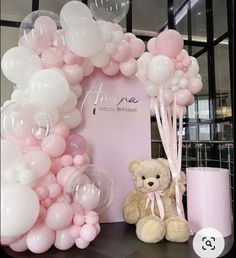 a teddy bear sitting in front of a balloon arch with pink and white balloons on it