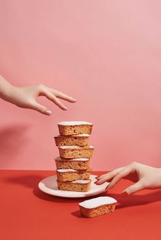 two hands reaching for a stack of cupcakes on a pink plate against a pink background