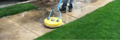 a man using a yellow and blue machine to clean the sidewalk in front of his house